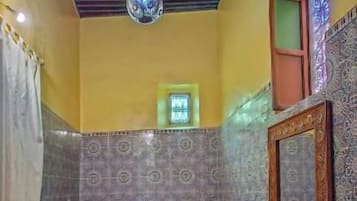 A room with two beds, a hanging light fixture, patterned walls, and a tiled floor.
