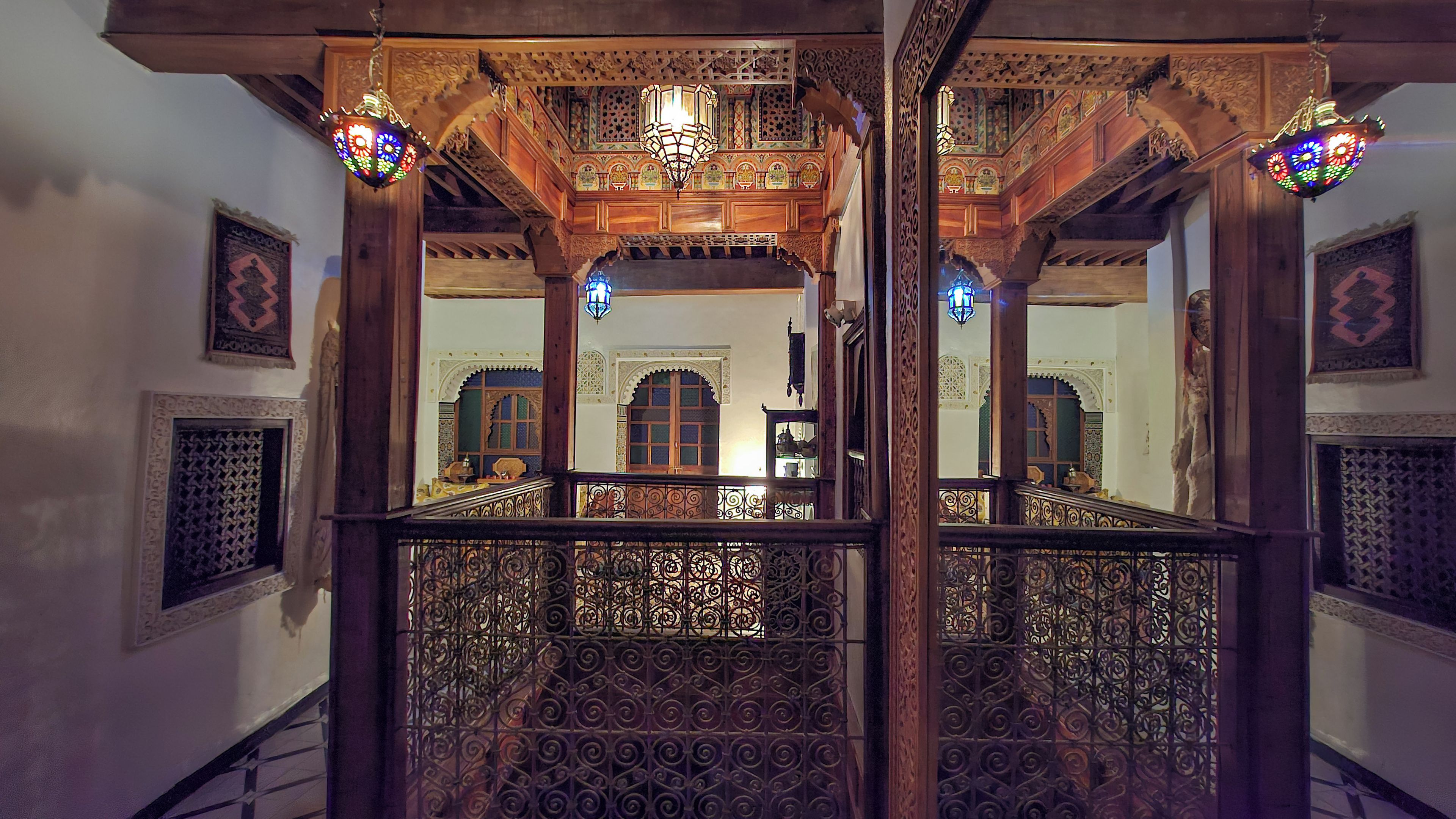 Una escalera de madera ornamentada con barandillas metálicas intrincadas y un muro espejado que refleja el interior.