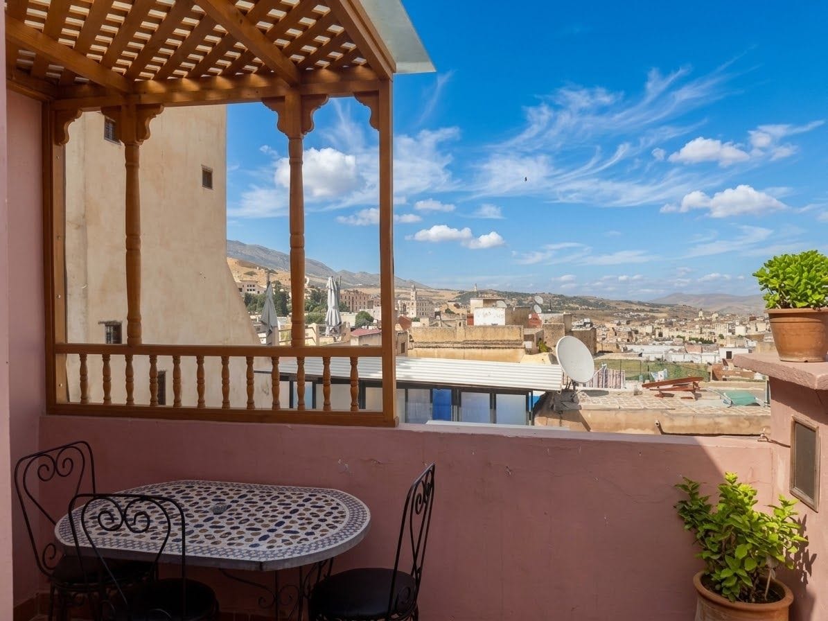 Un balcon avec une table et des chaises, un pot de fleurs et une vue sur le paysage urbain.
