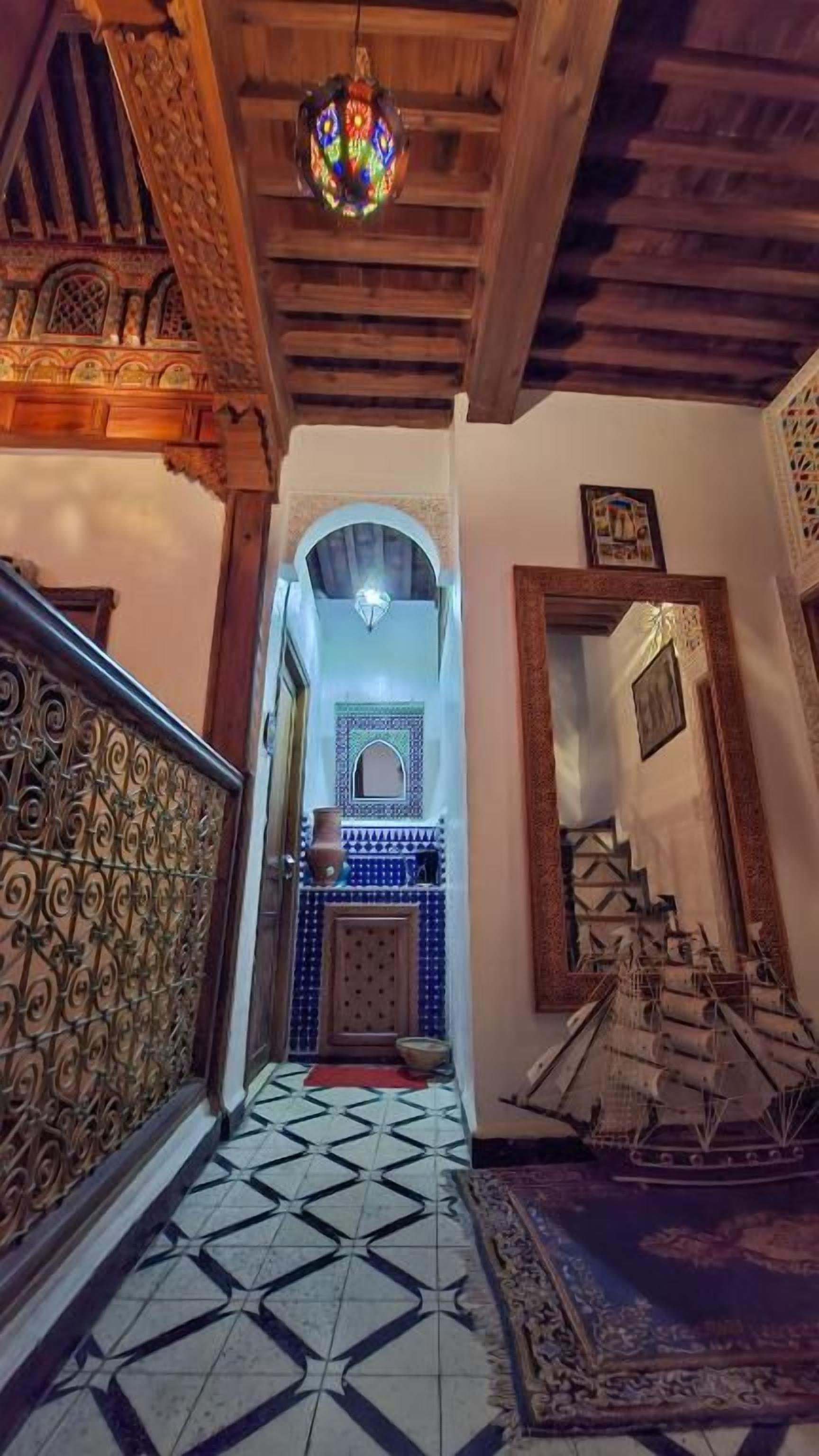 A hallway with a patterned floor, a wooden railing, and a hanging light fixture.