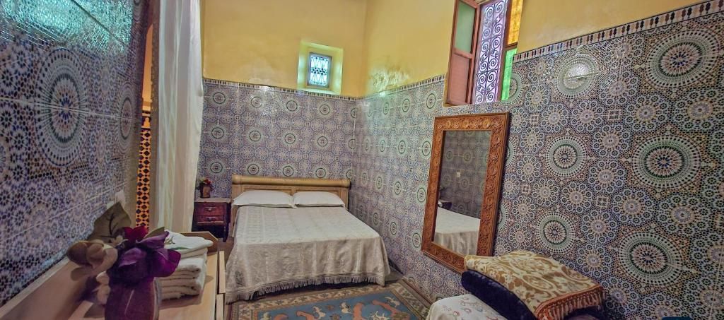 A bedroom with a bed, a nightstand, a mirror, and patterned walls.