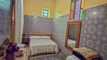 A bedroom with a bed, a nightstand, a mirror, and patterned walls.