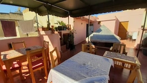 Un patio techado con una mesa, sillas, plantas en macetas y una cama.