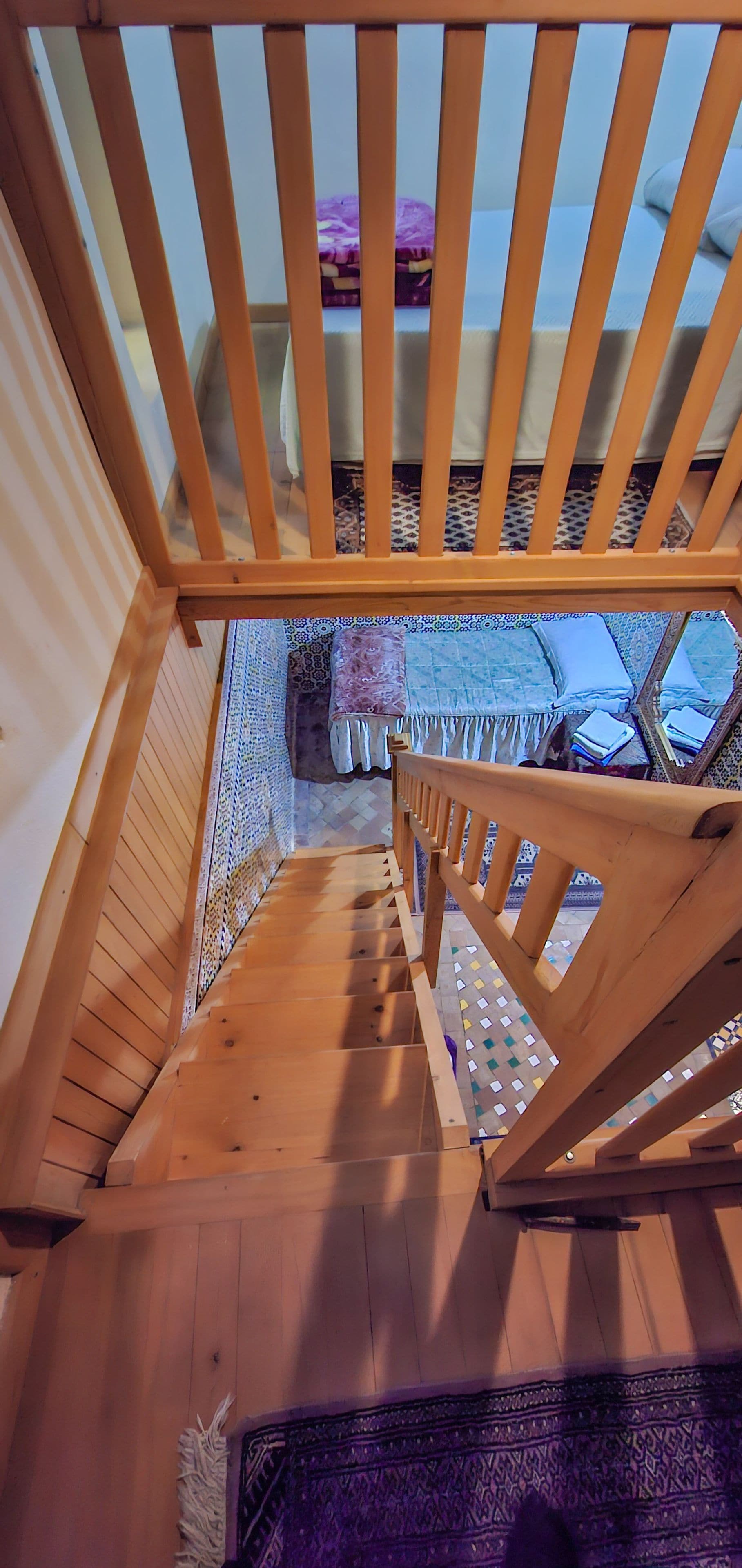 Eine Holztreppe mit Geländer führt zu einem Raum mit gemusterten Bodenfliesen.