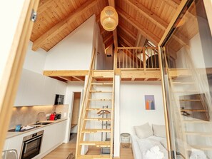 Un espai tipus loft amb una escala de fusta, una zona de cuina i un saló amb sofà.