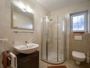 Ein modernes Badezimmer mit einer Duschkabine aus Glas, einem weißen Waschbecken, einer Toilette und einem Fenster.