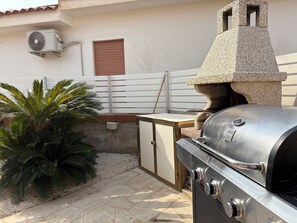 Eine Terrasse mit einem Grill, einem Steinkamin und einer Palme.