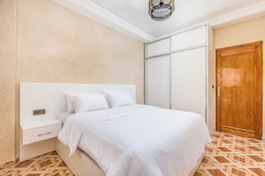 A bedroom with a bed, a nightstand, a wooden door, and a patterned floor. - Dar Raha House of Rest—a cozy vacation rental with a garden and terrace (Aourir)