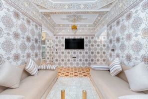 A room with patterned wallpaper, a sofa, a television, and a decorative ceiling. - Dar Raha House of Rest—a cozy vacation rental with a garden and terrace (Aourir)