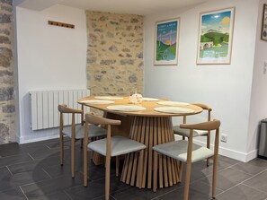 A dining area with a round wooden table, six chairs, and a radiator. - L'Oustal Del Nort - Vacation Rental for 6 People Near Millau (Aveyron) (Paulhe)