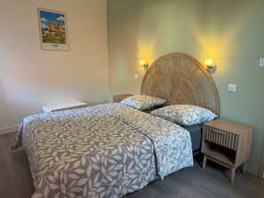 A bedroom with a bed, two bedside tables, a wicker headboard, and a wall-mounted picture of a cathedral. - L'Oustal Del Nort - Vacation Rental for 6 People Near Millau (Aveyron) (Paulhe)