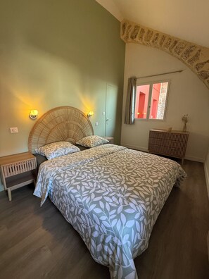 A bedroom with a bed, two bedside tables, a wall-mounted light fixture, a window with curtains, and a radiator. - L'Oustal Del Nort - Vacation Rental for 6 People Near Millau (Aveyron) (Paulhe)