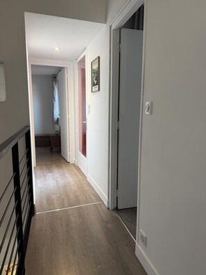 A hallway with a wooden floor, white walls, and a door leading to another room. - L'Oustal Del Nort - Vacation Rental for 6 People Near Millau (Aveyron) (Paulhe)