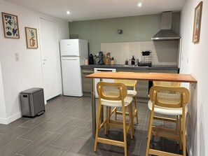 A compact kitchen with a white refrigerator, a stainless steel range hood, and a wooden table with two chairs. - L'Oustal Del Nort - Vacation Rental for 6 People Near Millau (Aveyron) (Paulhe)