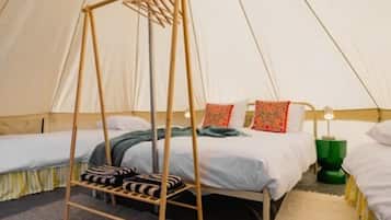 A tent-style room with two beds, a hanging chair, and a green bedside lamp.