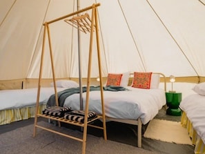 Een tentkamer met twee bedden, een hangstoel en een groene bedlamp.