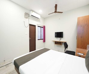 A hotel room with a bed, a desk with a television, a ceiling fan, and an air conditioning unit. - Villa Tian by Palette Homes (Chennai)