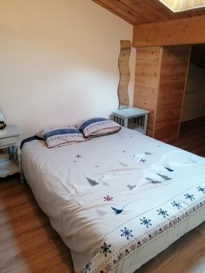 Une chambre avec un plafond en bois, un lit recouvert d ’une courtepointe blanche ornée de motifs de feuilles, deux oreillers, une table de chevet et une petite table.