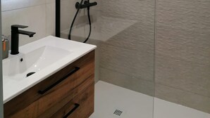 A modern bathroom with a white sink, wooden vanity, and a glass-enclosed shower area. - Vrbo Property (Saint-Chaffrey)