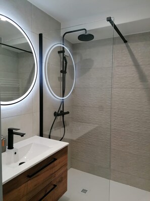 Une salle de bain moderne avec un lavabo blanc, un meuble-lavabo en bois et une douche séparée par une paroi de verre.