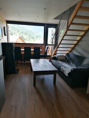 Une pièce avec une table en bois, un canapé, un escalier et une vue sur une zone boisée.
