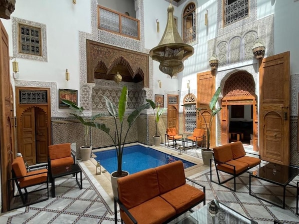En traditionell marockansk inredning med en pool, sittplatser och utsmyckad dekor.