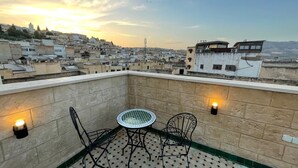 Terraço no telhado com uma mesa redonda e duas cadeiras, cercado por paredes de pedra e um chão estampado.