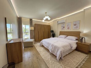 Une chambre à coucher avec un lit, des tables de chevet, un miroir, une armoire et une fenêtre avec des rideaux.