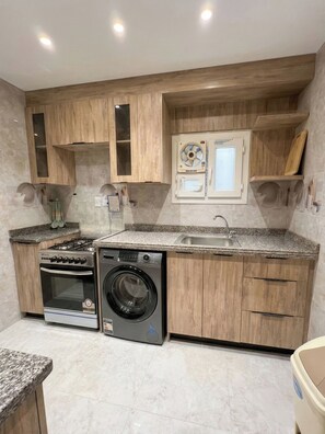 Une cuisine compacte avec des meubles en bois, une cuisinière à gaz, un lave-linge encastré et un évier.