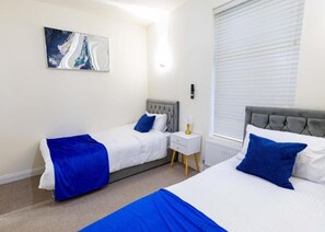 Ein Hotelzimmer mit zwei Betten, einem Nachttisch, einer Wandlampe und einem Fenster mit Jalousien.