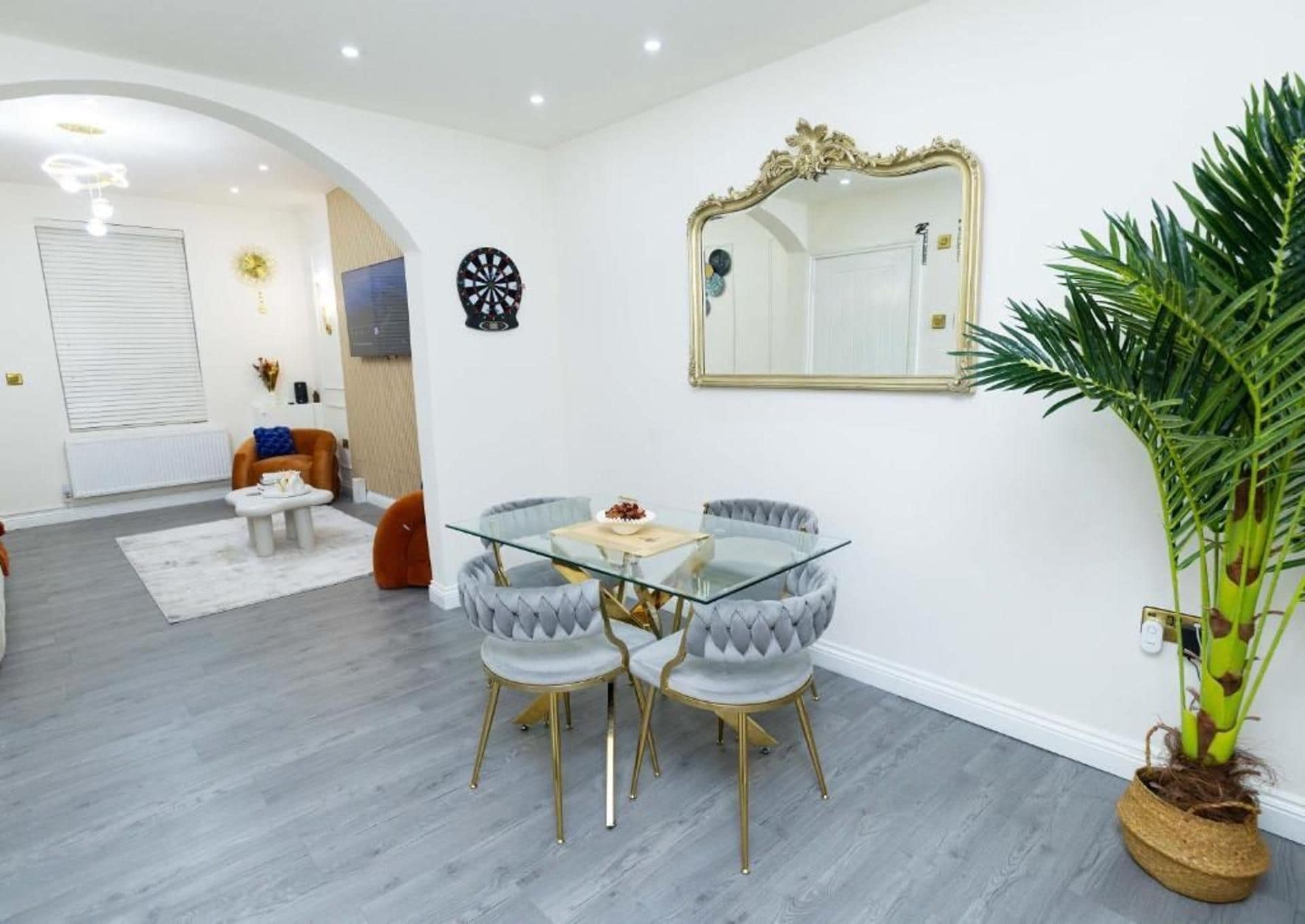 Uma área de jantar moderna com mesa de vidro e cadeiras estofadas, um espelho grande e um vaso com planta.