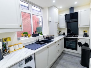 A modern kitchen with white cabinets, a black sink, and a built-in oven. - Cosy 3 Bedroom House In Manchester Sleeps 7 (Salford)