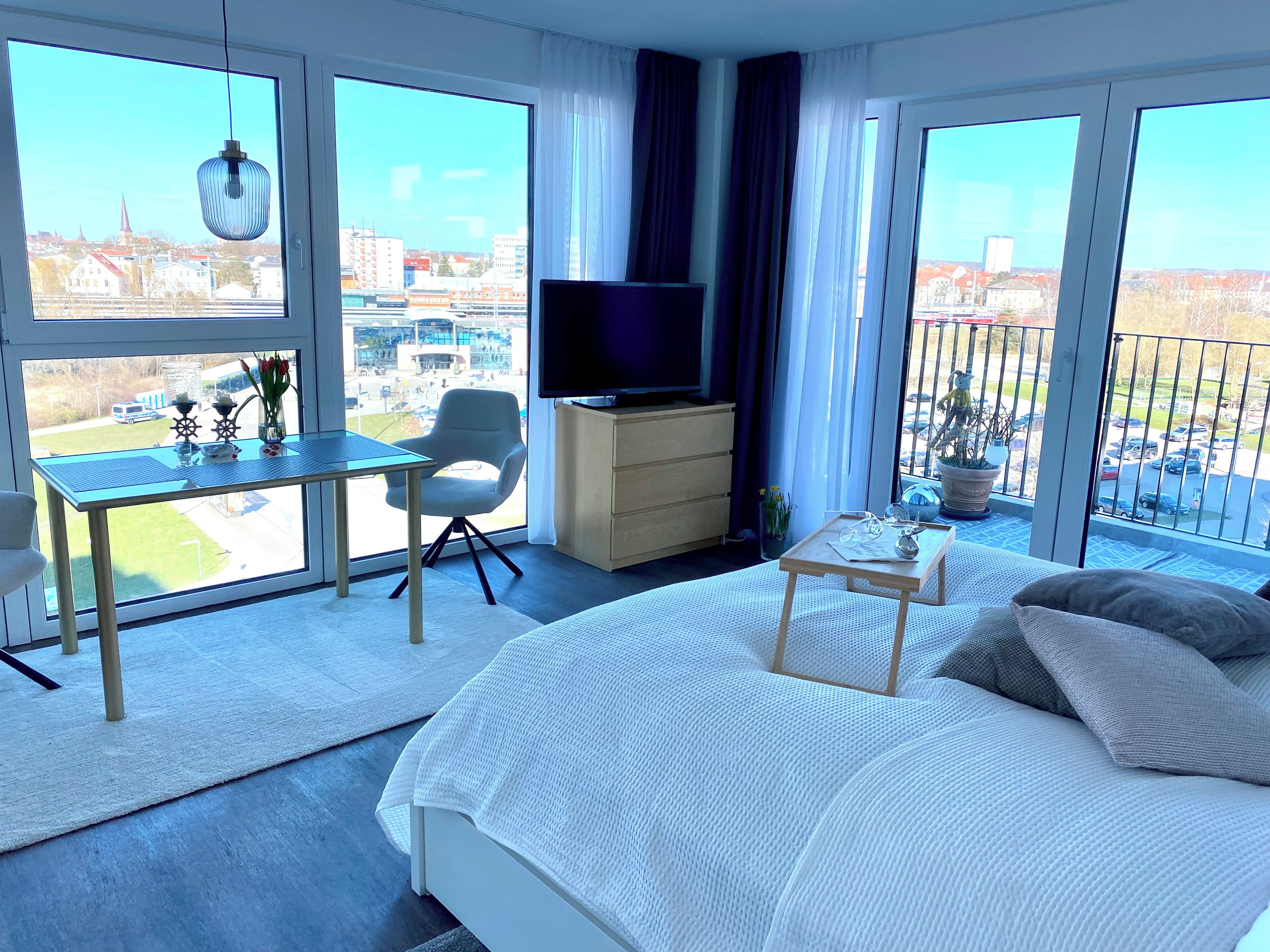 A hotel room with a bed, a desk, a chair, a television, and large windows offering a city view.