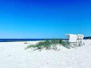 Ein Strand mit weißen Korbstühlen und blauem Himmel.