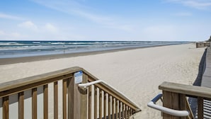Una passerella in legno conduce a una spiaggia sabbiosa sotto un cielo sereno.