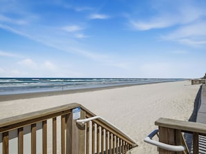 Une promenade en bois mène à une plage de sable fin, sous un ciel dégagé.