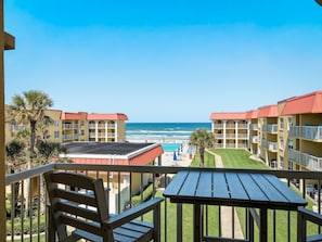 Un balcon donnant sur une plage, une piscine et un immeuble doté de nombreux balcons.