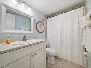 A bathroom with a sink, mirror, toilet, and shower curtain. - Top-Floor Condo | Direct Ocean Views | Non-Driving Beach (New Smyrna Beach)
