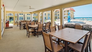 Un'area pranzo all'aperto coperta con tavoli e sedie, una piscina e vista sulla spiaggia.