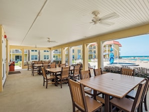 Un espace extérieur abrité, aménagé pour les repas, avec des tables et des chaises, une piscine et une vue sur la plage.