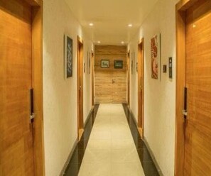 A hotel hallway with wooden doors, a tiled floor, and framed pictures on the walls. - Deluxe Room Riboila (Indore)