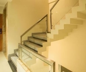 A staircase with glass railings and a handrail, leading to an upper floor. - Deluxe Room Riboila (Indore)