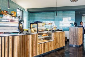 A bakery counter with a display case, a coffee machine, and a wooden counter. - Luxury 2-Bed Flat w/ Rooftop Pool & Gym (Nairobi)