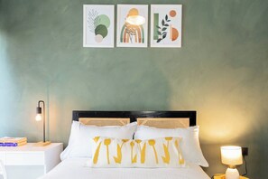 A bed with white bedding and two pillows, a bedside table with a lamp, and three framed artworks on the wall. - Luxury 2-Bed Flat w/ Rooftop Pool & Gym (Nairobi)
