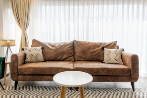 A brown leather sofa with two patterned pillows, a white round table, and a floor lamp. - Luxury 2-Bed Flat w/ Rooftop Pool & Gym (Nairobi)