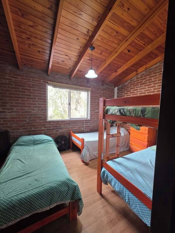 Une pièce avec des lits superposés en bois, une fenêtre et un ventilateur.