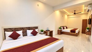 A hotel room with a large bed, a smaller bed, a desk, a chair, a plant, and a wardrobe. - Shree Radhe Shyam Palace (Khatoo)