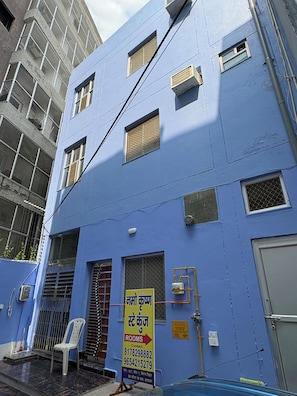 A multi-story building with a blue exterior, multiple windows, and a sign indicating rooms for rent. - Namo Krishn Stay Kunj (Mathura)
