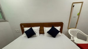 A single bed with a wooden headboard, two pillows, a white chair, and a mirror on the wall. - Namo Krishn Stay Kunj (Mathura)