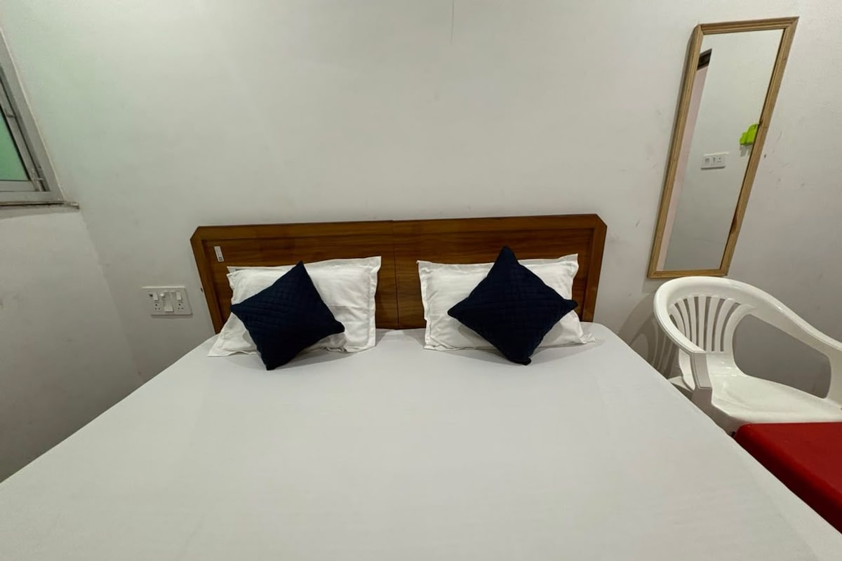 A single bed with a wooden headboard, two pillows, a white chair, and a mirror on the wall.